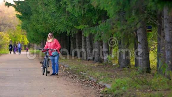 女人带着自行车在公园里散步她去看远处的摄像机视频的预览图