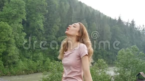 美丽的幸福女孩站在夏雨中在群山覆盖的森林的背景下年轻女子视频的预览图