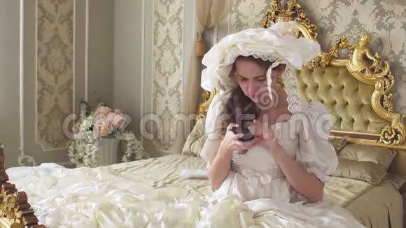 穿着球服的年轻女子坐在金色装饰的床上手机上写着短信公主用小玩意视频的预览图