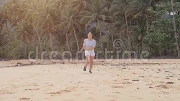 快乐的旅行者女孩在美丽的粉红色夕阳下在空荡荡的海滩上奔跑跳跃和笑声充满了快乐旅行博主视频的预览图