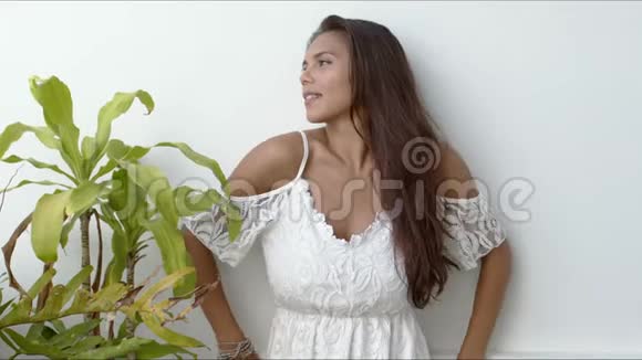 穿着白色连衣裙的红发女郎站在绿色植物旁边视频的预览图
