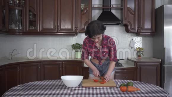 美丽的微笑着的年轻女孩穿着一套针装在现代舒适的厨房里在木板上切菜视频的预览图