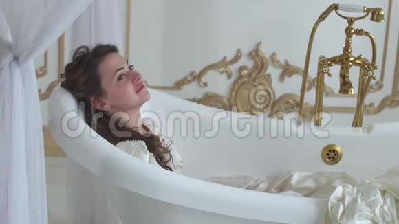 年轻的微笑的女人躺在老式浴室的浴室里穿着一件紧身的球袍视频的预览图