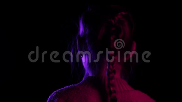 十几岁的女孩在霓虹灯的黑色背景上转过身来在黑暗的摄影棚里寻找镜头的肖像少女视频的预览图