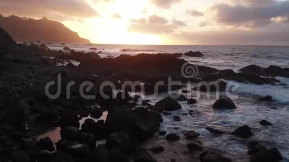 空中飞行日落时分海滩景色向黑石和火山沙开放黄金时刻摄像机向前移动视频的预览图