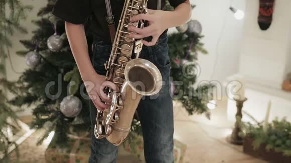 孩子带着乐器的男孩在圣诞装饰的背景下演奏萨克斯管音乐的男孩视频的预览图
