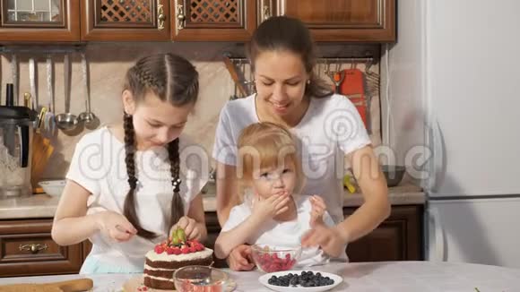 一家人妈妈带着两个小女儿在家里的厨房里一起装饰生日蛋糕和浆果视频的预览图