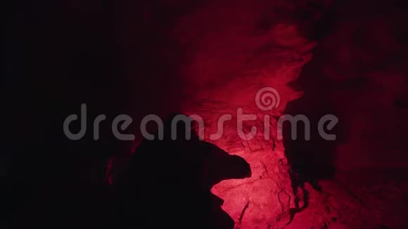 人走在神秘的地下洞穴里黑暗的墙壁背景上有一个红色的燃烧信号耀斑库存数据视频的预览图