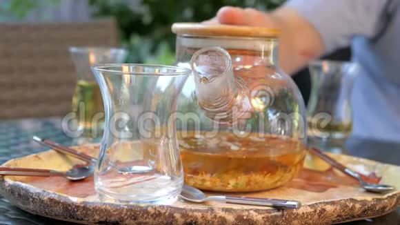 一个人手把茶从一个玻璃茶壶倒入一个杯子里视频的预览图