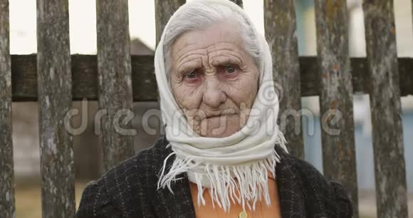 一位年长的女人在一条旧栅栏的背景下围巾上有深深的皱纹视频的预览图