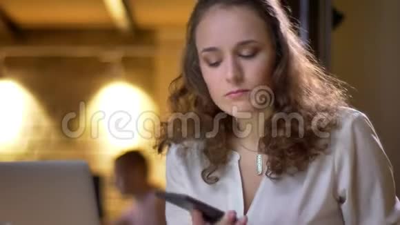 卷发女人在办公室里同时用手机和笔记本做笔记的特写照片视频的预览图