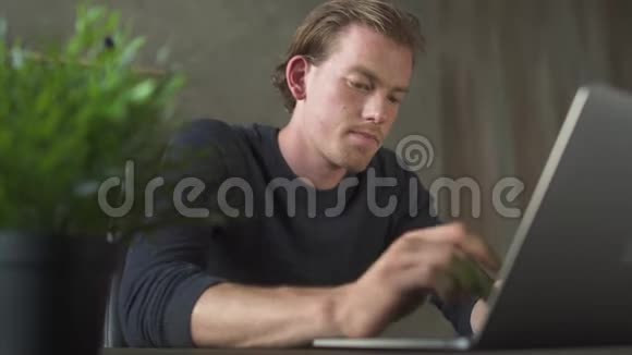 年轻的金发忧心忡忡的男人坐在办公室的桌子上在笔记本上工作英俊的商人在笔记本电脑上打字视频的预览图