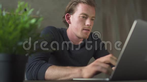 快乐的微笑年轻商人坐在电脑前在笔记本电脑上打字一个英俊的商人发短信视频的预览图