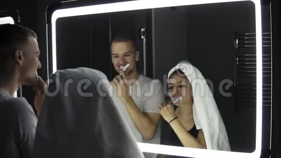 年轻的情侣在室内刷牙时照镜子女士头上戴着浴巾关门视频的预览图