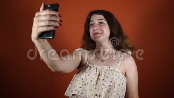 一个穿裙子的女人在橙色自拍带电话的女性视频的预览图