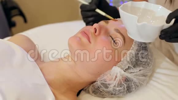 美容师在水疗沙龙中将水凝胶应用于年轻女性的面部视频的预览图