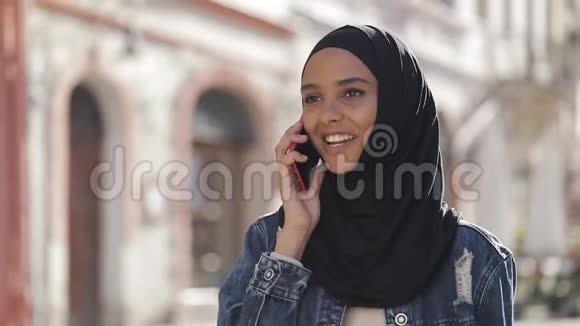 年轻的穆斯林妇女戴着头巾在城市的智能手机上和朋友交谈一位女士沿着一位老女士走着视频的预览图
