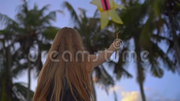 日落时分一名带风筝的年轻女子在热带海滩上慢镜头拍摄视频的预览图