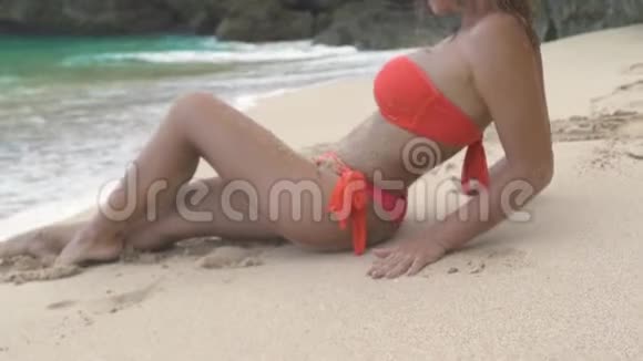 美丽的女人放松在沙滩上的蓝色海洋和悬崖景观穿比基尼的漂亮女人躺在沙滩上视频的预览图