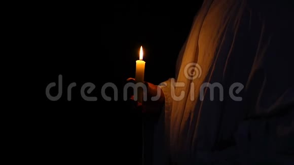 穿长袍的人在黑暗的背景下手持燃烧的蜡烛视频的预览图