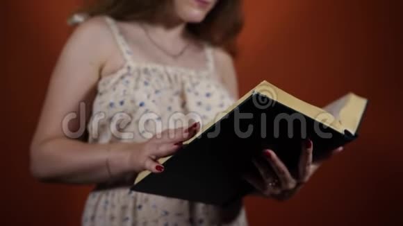 女性在橙色背景下阅读一本书女人翻阅一本大书视频的预览图