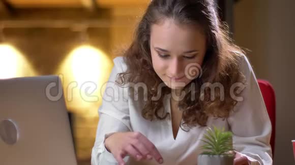 一位卷发女商人的特写肖像她专心地在办公室里同时使用笔记本电脑和智能手机视频的预览图