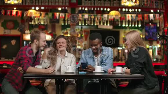 欢快的年轻朋友坐在咖啡馆里看智能手机的肖像各种种族的人坐在餐桌前视频的预览图
