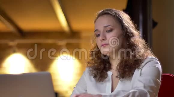 一位年轻的卷发女人无聊而疲惫地躺在椅子上在办公室里摇着头发的特写肖像视频的预览图