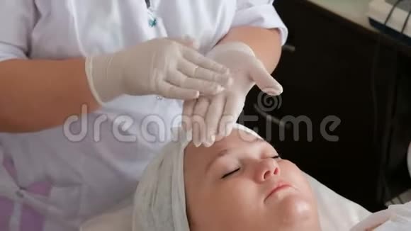 戴着白手套的专业美容师的双手在一个女人脸上涂上奶油对女人的满意视频的预览图