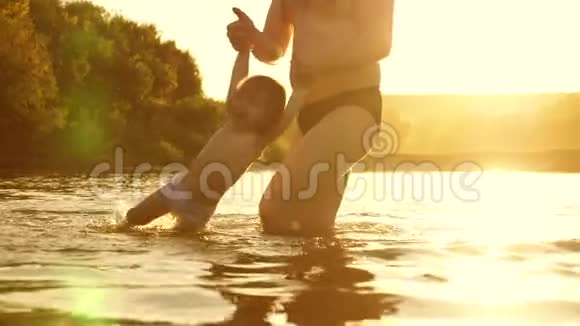 快乐的爸爸和快乐的微笑的宝宝在金色的夕阳下在水中洗澡和玩耍爸爸和小女儿在玩视频的预览图