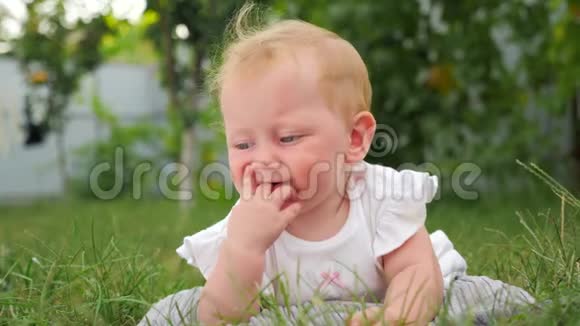 活跃的婴儿背景幼儿牙齿问题小女孩躺在绿草上前花园背景视频的预览图