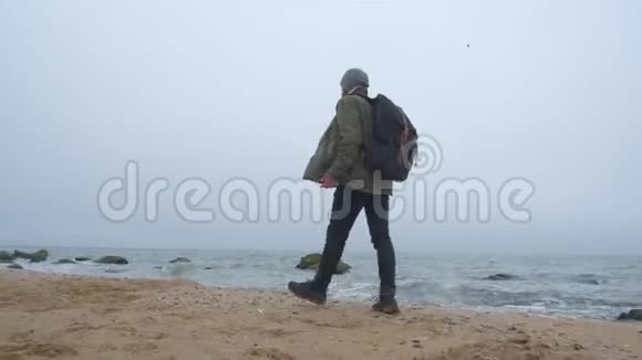 一个带背包的有胡子的时髦旅行者沿着海滩散步视频的预览图
