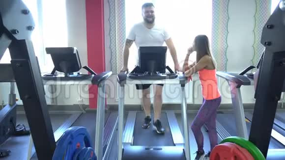 肥胖的白种人男子在健身房的跑步机上行走女教练监控练习的正确性视频的预览图