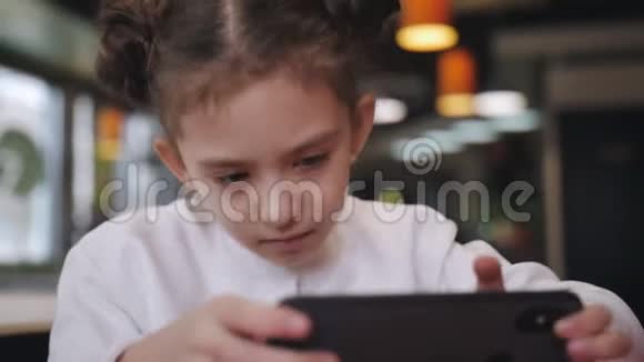 一个小女孩在咖啡馆的桌子上玩智能手机特写视频的预览图
