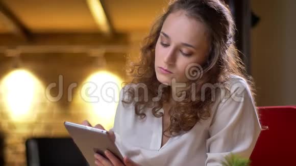 一幅年轻卷发女商人的画像她严肃地看着平板电脑抬起眼睛看着办公室里的照相机视频的预览图