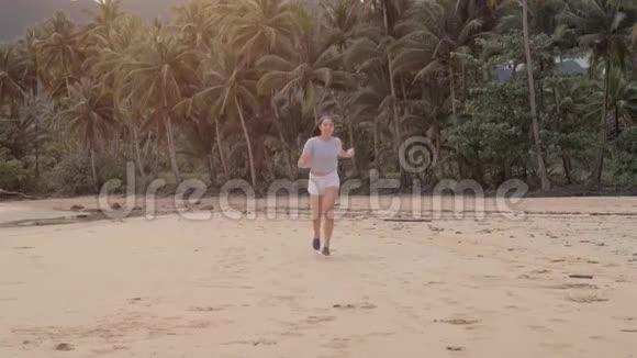 快乐的旅行者女孩在美丽的粉红色夕阳下在空荡荡的海滩上奔跑跳跃和笑声充满了快乐旅行博主视频的预览图