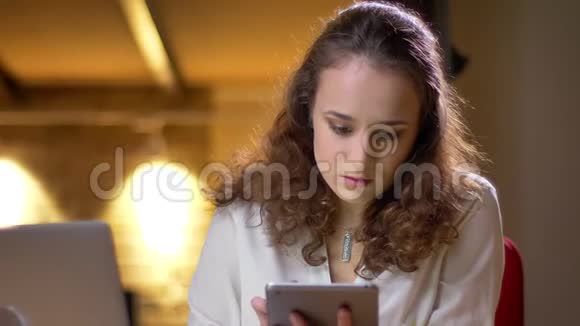 一位年轻的卷发女商人的特写肖像观看平板电脑并将其绿色屏幕显示给相机视频的预览图