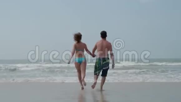 一个年轻人和一个女孩正高兴地牵着手跑进大海4K视频的预览图
