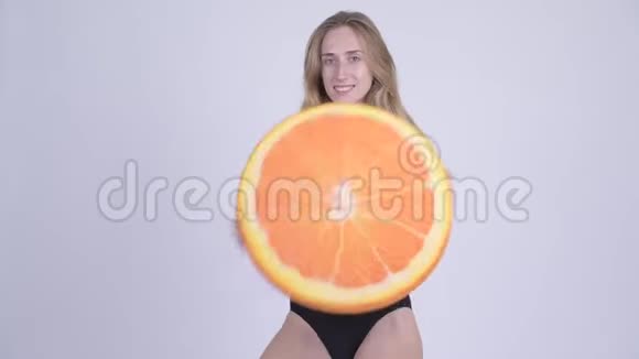 穿着泳衣咬着橙色枕头的年轻金发美女健康的概念视频的预览图