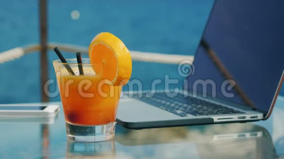 女人手在笔记本电脑键盘上打字笔记本电脑站在俯瞰大海的桌子上关上鸡尾酒视频的预览图