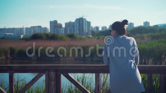 一个年轻的女孩站在湖岸上背景是城市景观和蓝天视频的预览图