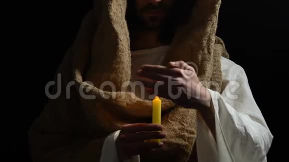 耶稣基督穿着长袍在黑暗的背景下拿着燃烧的蜡烛视频的预览图
