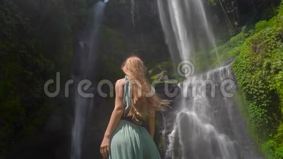 年轻女性游客参观巴厘岛最大的瀑布塞库普尔瀑布慢镜头旅费视频的预览图