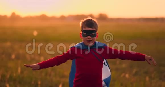 穿着超级英雄服装和面具的男孩在日落时跑过田野梦想着幻想视频的预览图