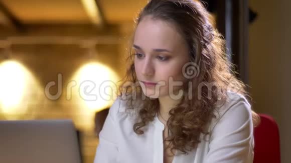 一位年轻的卷发女士在混乱中使用笔记本电脑她的特写镜头转向镜头微笑着看着视频的预览图