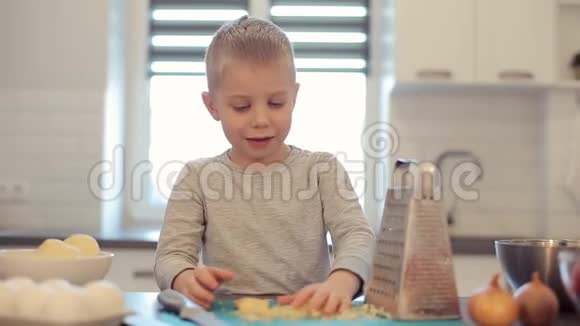 漂亮的白种人小男孩大蓝眼睛在明亮的厨房里做饭他是泼奶酪的奶酪烤炉视频的预览图