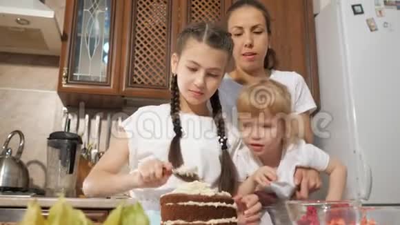 一家人妈妈带着两个小女儿在家里的厨房里一起装饰生日蛋糕和浆果视频的预览图