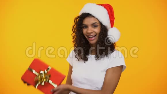 戴着圣诞帽戴着红色礼品盒和微笑的快乐混血女人视频的预览图