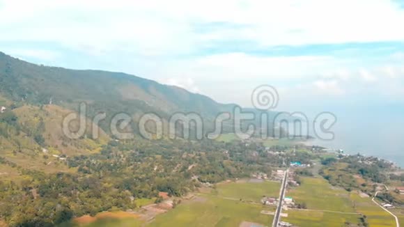 空中来自印度尼西亚苏门答腊岛上方的托巴湖和萨莫西尔岛巨大的火山岩覆盖着水巴塔克村绿色的视频的预览图