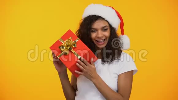 快乐的混血女人戴着圣诞帽手里拿着红色礼品盒跳舞度假视频的预览图